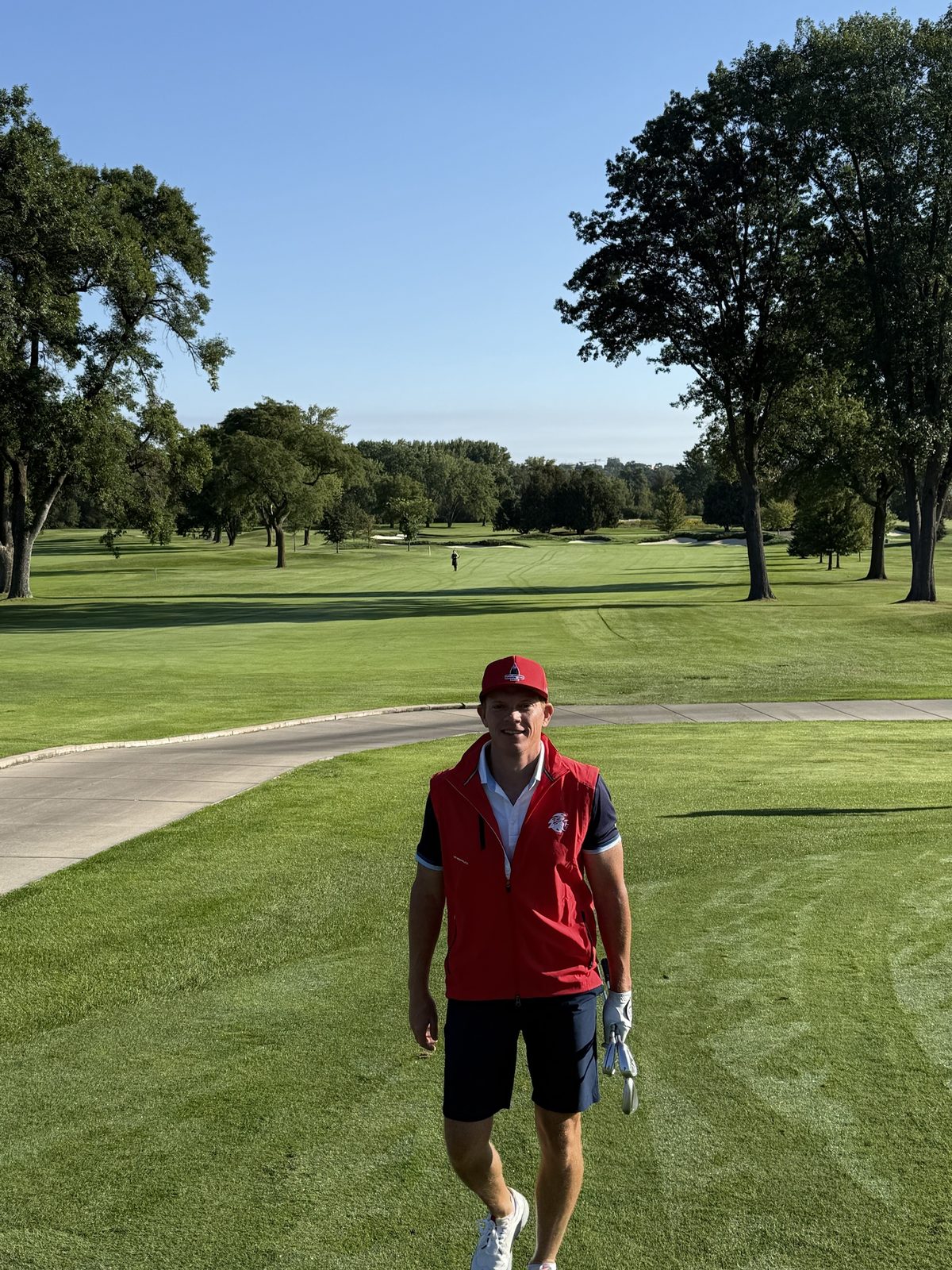 Player in a red vest walking up the fairway
